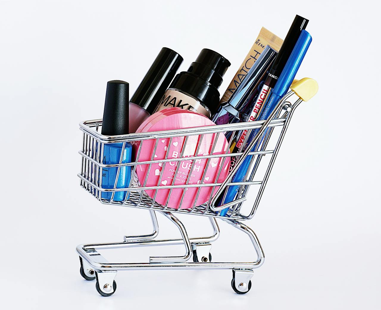 why-choose-us Miniature shopping cart filled with a variety of cosmetics on a white background.